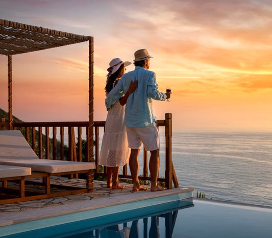 A man and woman standing on an overwater deck watching sunset over the ocean at a luxury resort