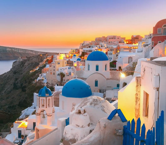 Sunset over whitewashed buildings with bright blue roofs on a dramatic cliff at a luxury hotel in Santorini, Greece
