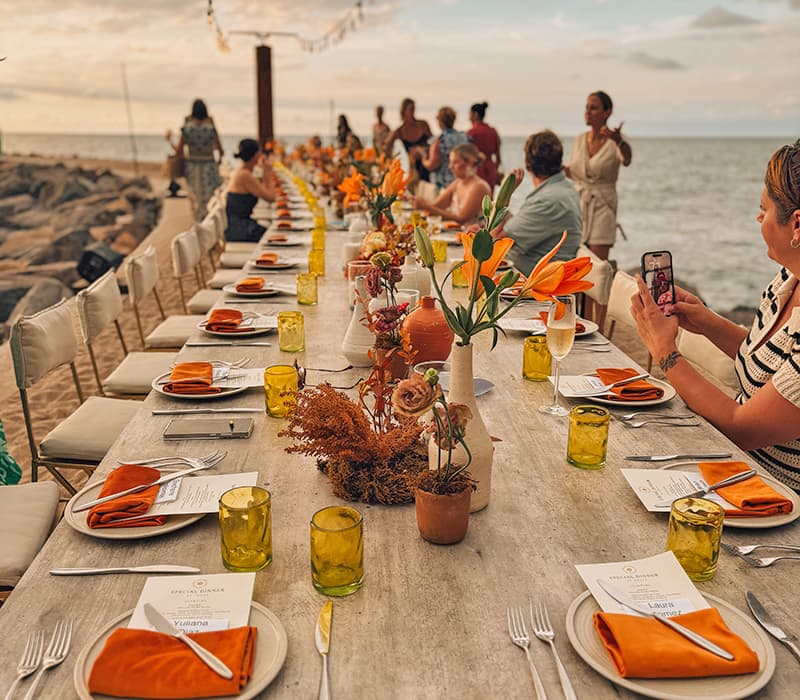 A group of people at a long table on a beach at sunset at a Nellie corporate offsite
