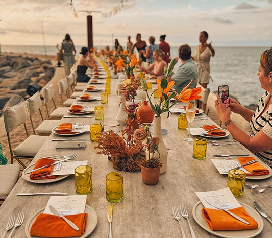 A group of people at a long table on a beach at sunset at a Nellie corporate offsite