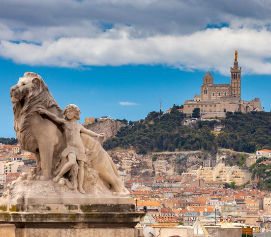 Statue of a lion and child in front of a cityscape in Southern France, with a castle on a hill in the background